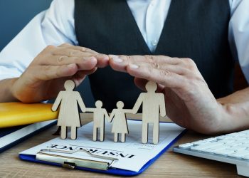 Agent protects family figures. Life Insurance policy on a desk.